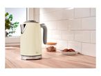 Cream-colored electric kettle on a wooden kitchen countertop next to cookies and a jar