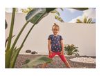 Young girl in a dark blue strawberry print t-shirt and red leggings, standing outdoors.