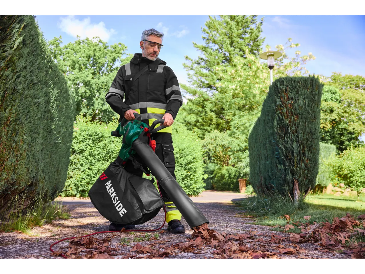 Man uses a Parkside® leaf blower to clear leaves from a path.
