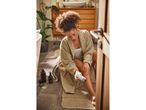A woman in a bathrobe epilating her leg in a bathroom.