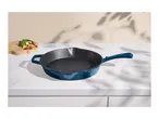 Blue cast iron frying pan on a white marble countertop with vegetables on a wooden board.