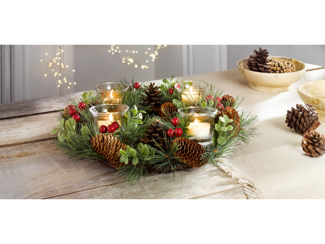 LIVARNO home Christmas Wreath with pinecones, red berries, and four lit candles on a wooden table.