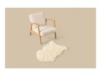 A beige upholstered armchair with wooden legs and armrests next to a fluffy white rug.