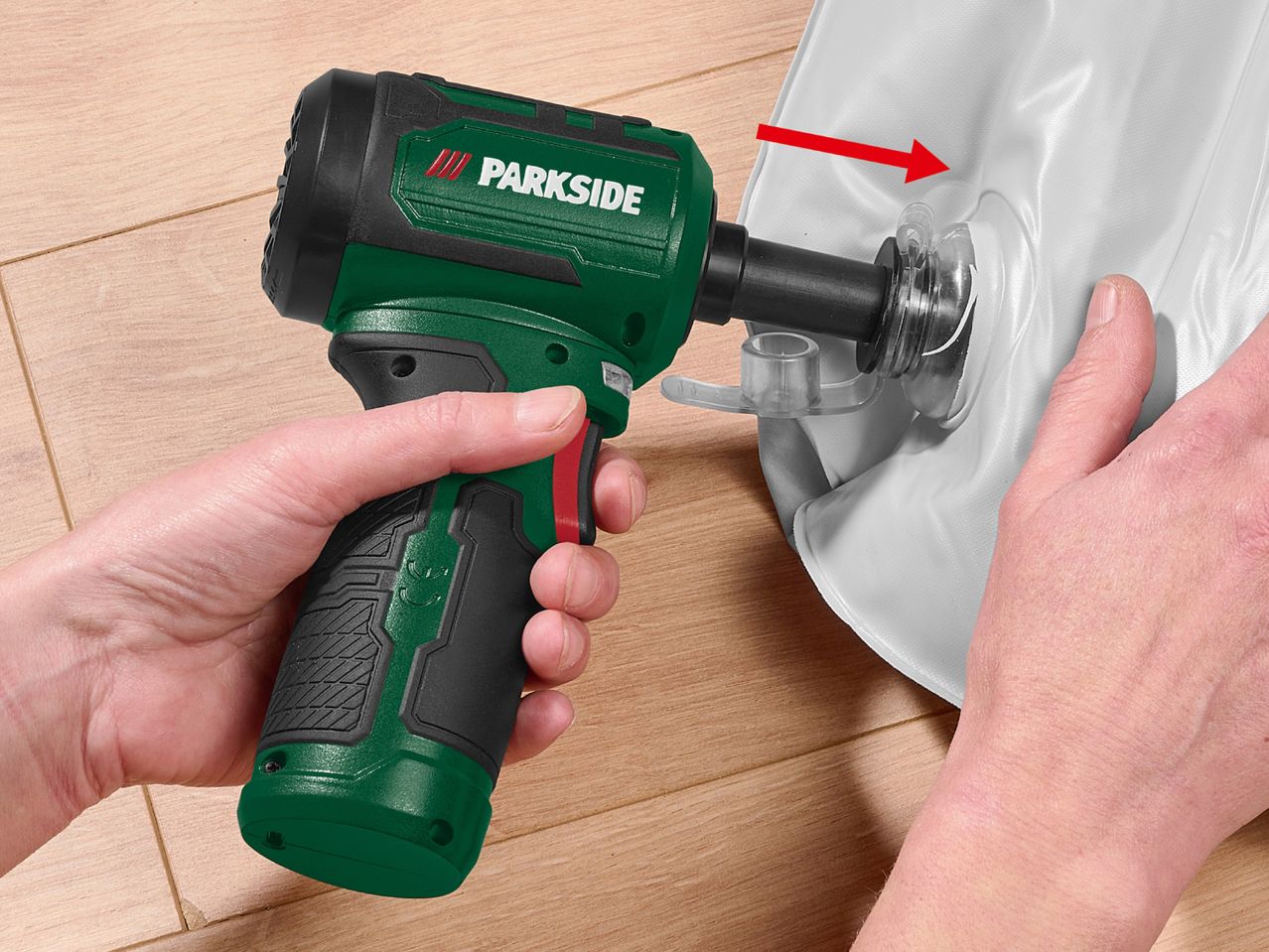 A person using a green and black power tool to inflate a white inflatable item.