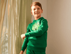 Ein lächelnder Junge in einem grünen Minecraft-Hoodie steht vor einem Vorhang.