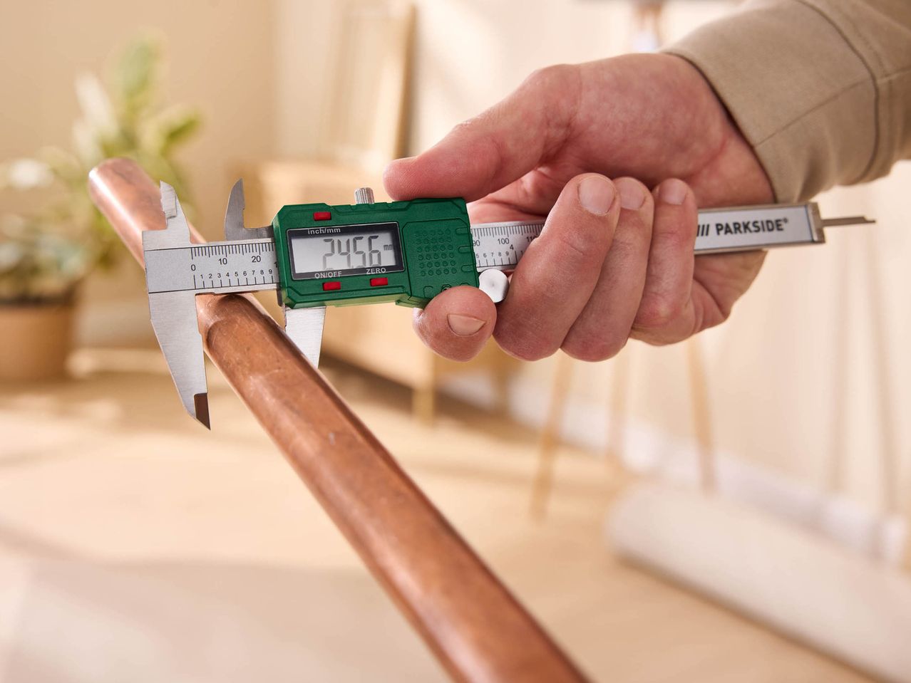 A person measuring a copper pipe with a Parkside digital caliper, displaying 24.56 mm.