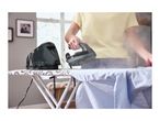 A person using a steam generator iron to iron a blue shirt on an ironing board.