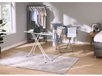 Estendal de roupa e tábua de engomar com ferro numa sala iluminada.