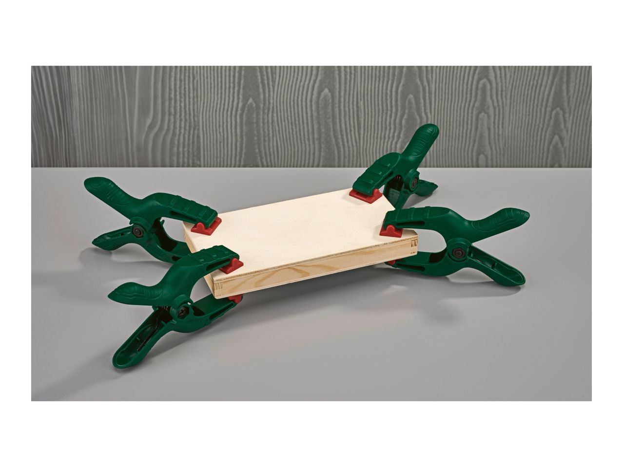 Four green spring clamps holding together two pieces of light wood.