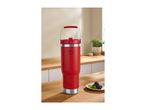 Red insulated tumbler with a handle on a wooden kitchen counter with blackberries.