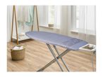 Ironing board with a blue cover, laundry basket, and clothes rack in a bright room.