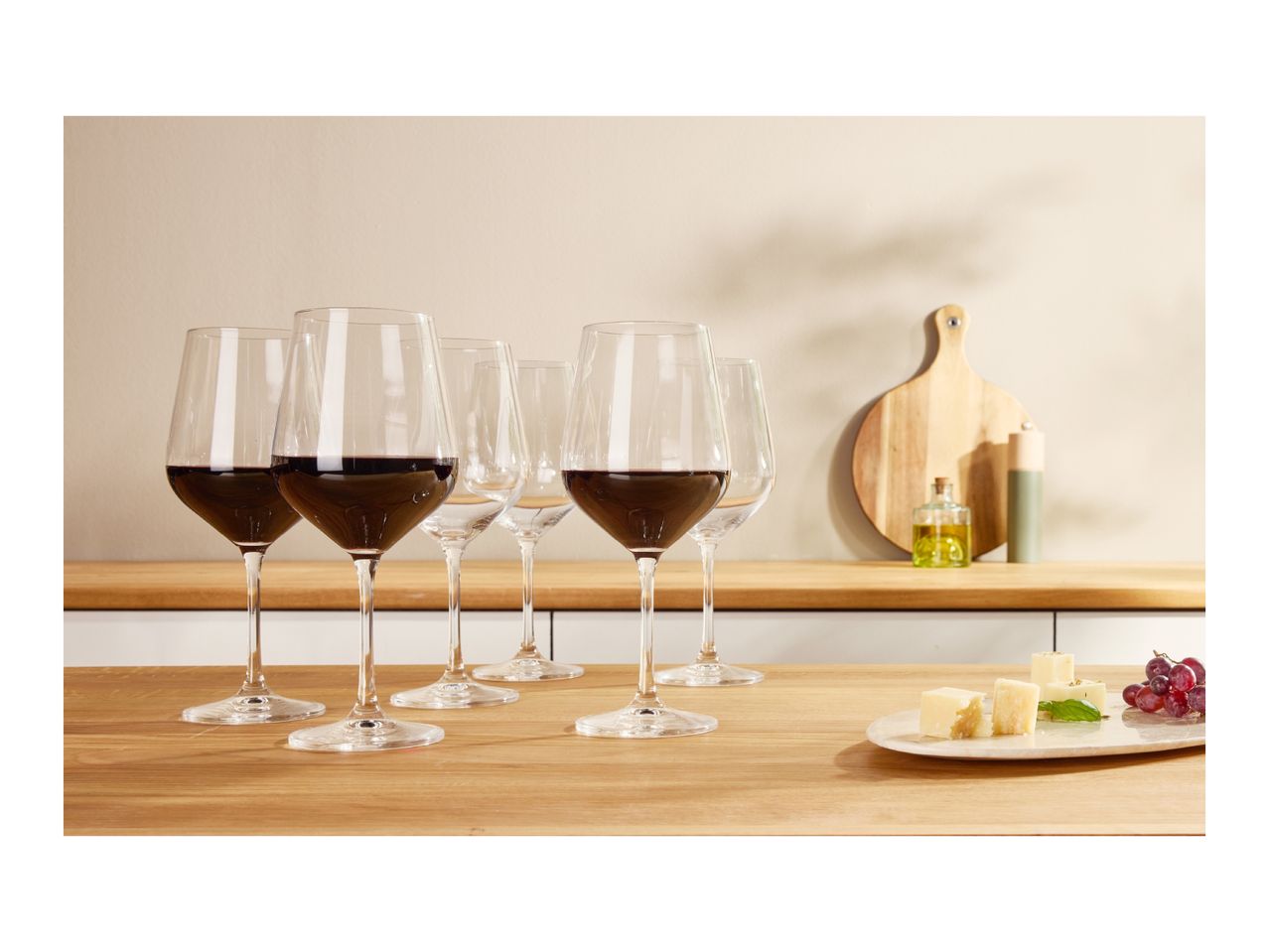 Red wine glasses on a wooden counter with cheese and grapes.