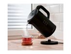 Black electric kettle pouring hot water into a glass cup of tea on a wooden counter.