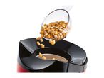 Popcorn kernels being poured from a measuring cup into a red and black popcorn maker.