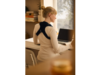 Woman wearing a posture corrector while working on a laptop at a desk.