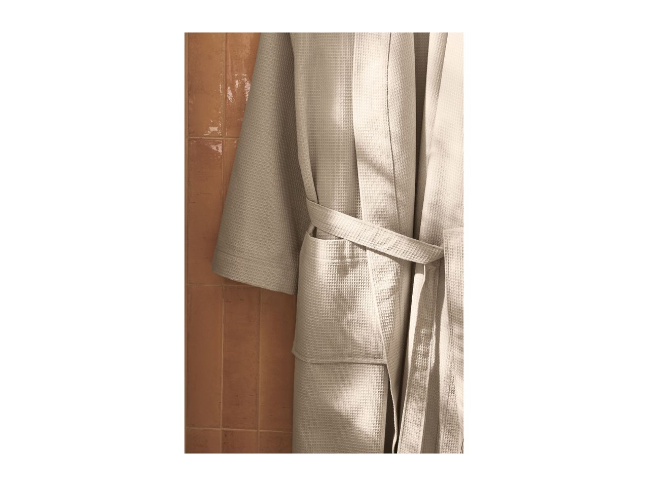 Light beige waffle-knit bathrobe hanging on a terracotta tiled wall.