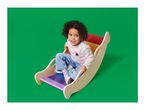 A child with curly hair sits in a wooden rainbow-colored rocker, smiling at the camera.