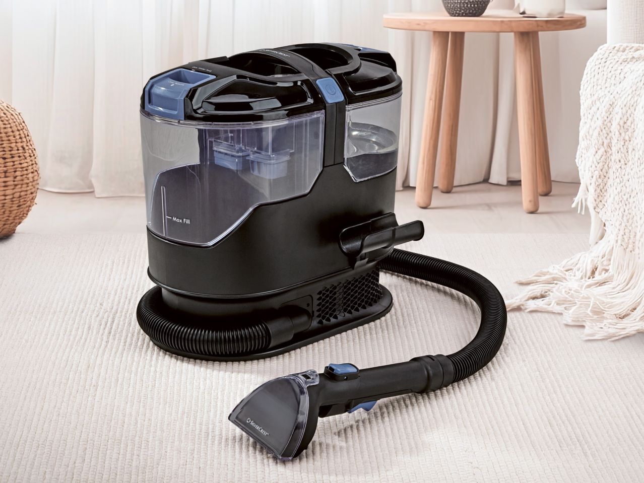 A black and clear carpet cleaner with a hose and nozzle on a white textured rug.
