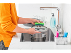 A woman washes a pot and lid in the kitchen.
