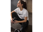 A woman rests after a workout, holding a Nike water bottle while wearing Nike leggings and a t-shirt.