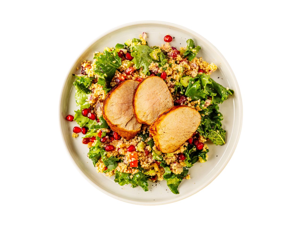Pork tenderloin with couscous, kale, and pomegranate salad on a white plate.