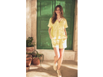Mulher de camisa amarela de manga curta e calções a condizer, a sorrir em frente a uma porta verde.