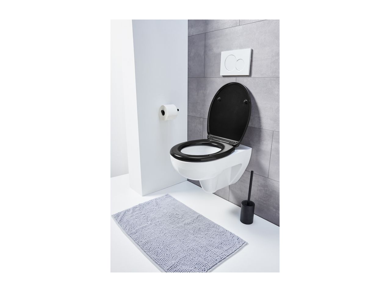 A modern bathroom with a wall-mounted toilet, black seat, toilet brush, and a gray bath mat.
