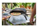 Outdoor pizza oven with a fresh pizza being removed by a pizza peel in a garden setting.
