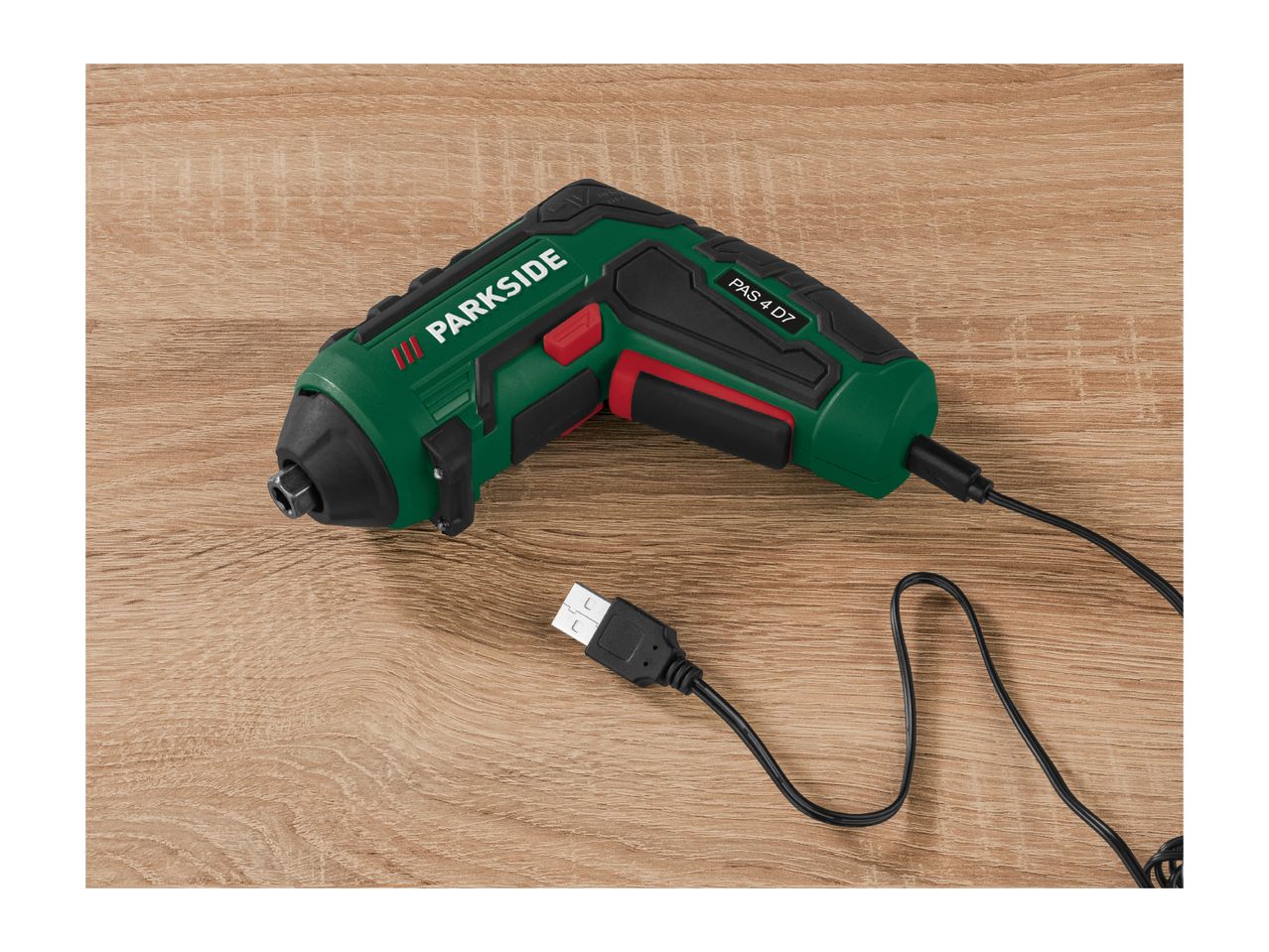 A green and black Parkside PAS 4 D7 cordless screwdriver with a USB charging cable on a wooden surface.
