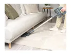 Person vacuuming under a light grey sofa with a cordless stick vacuum cleaner.
