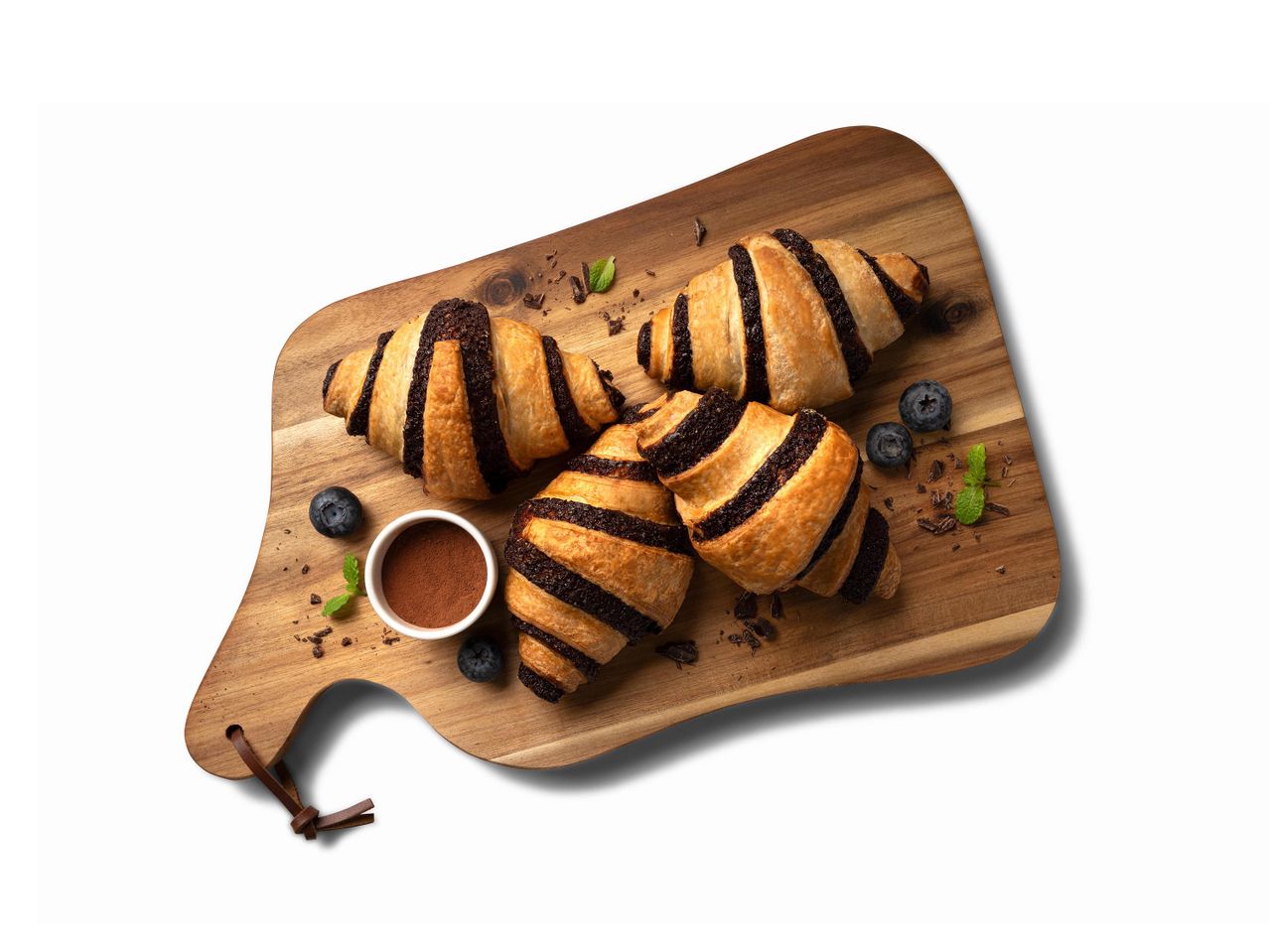 Csokoládés croissant-ok áfonyával és kakaóporral egy fa vágódeszkán.