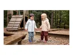 Two happy children in waterproof jackets and trousers splashing in a puddle.