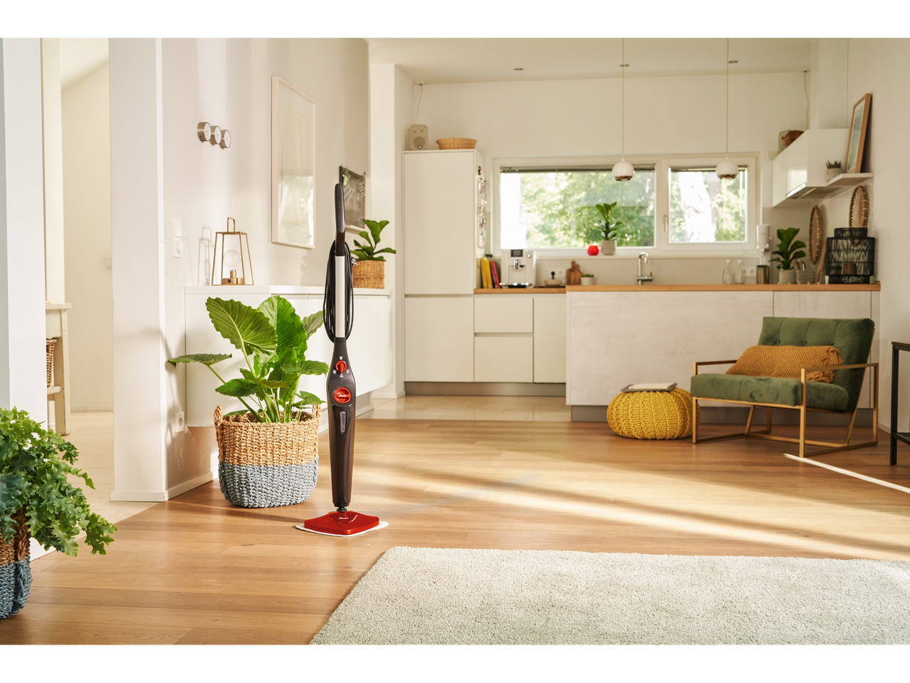 A steam mop stands on a wooden floor in a modern kitchen and living area.