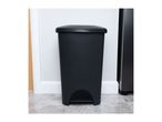 Black pedal bin with a lid on a patterned floor next to a white wall.