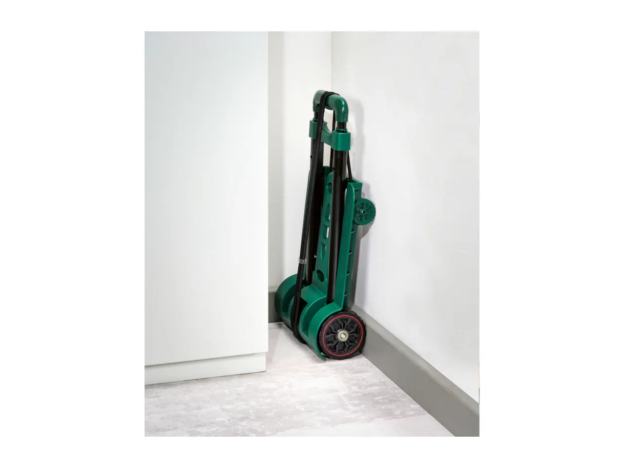 Folded green hand truck with black wheels and red accents, stored in a corner.