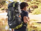 Man wearing a black and green CRIVIT hiking backpack by a lake.