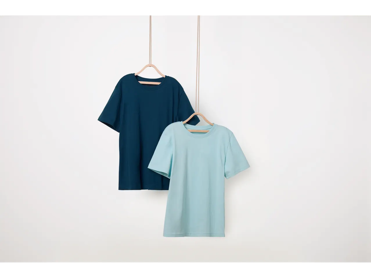 Δύο βαμβακερά t-shirt, ένα σκούρο μπλε και ένα ανοιχτό μπλε, κρεμασμένα σε ξύλινες κρεμάστρες.