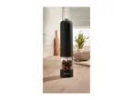 Black electric pepper grinder filled with peppercorns on a wooden kitchen counter.