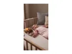 Baby in a pink sleepsuit lying in a wooden cot next to a glowing plush toy.
