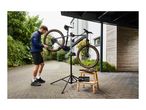 Man repairing a mountain bike on a repair stand with tools on a wooden stool.