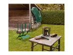 A green log sawhorse with a log, a wood splitter, and a hand saw on a wooden table in a garden.