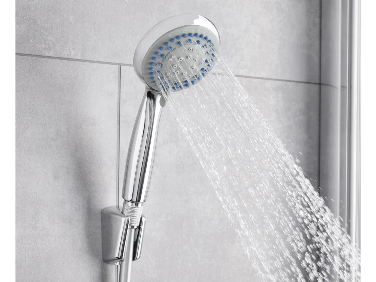 A chrome and white adjustable shower head sprays water against a tiled wall.