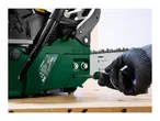 A gloved hand adjusting the chain tension of a green petrol chainsaw with a screwdriver.