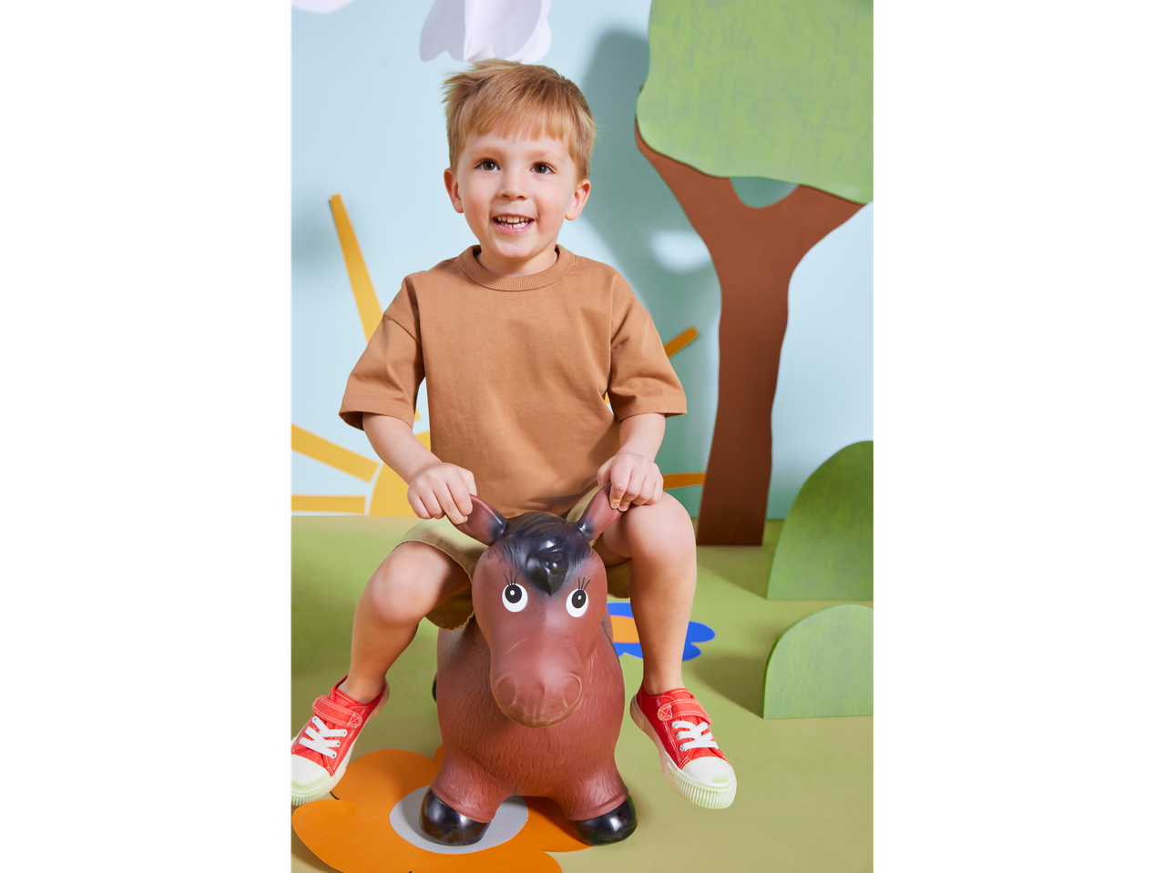 Um menino feliz brinca em um cavalinho de brinquedo em um cenário divertido.