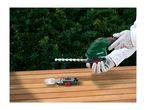 Person wearing gloves holding a hedge trimmer, with a grass shear attachment on a wooden table.