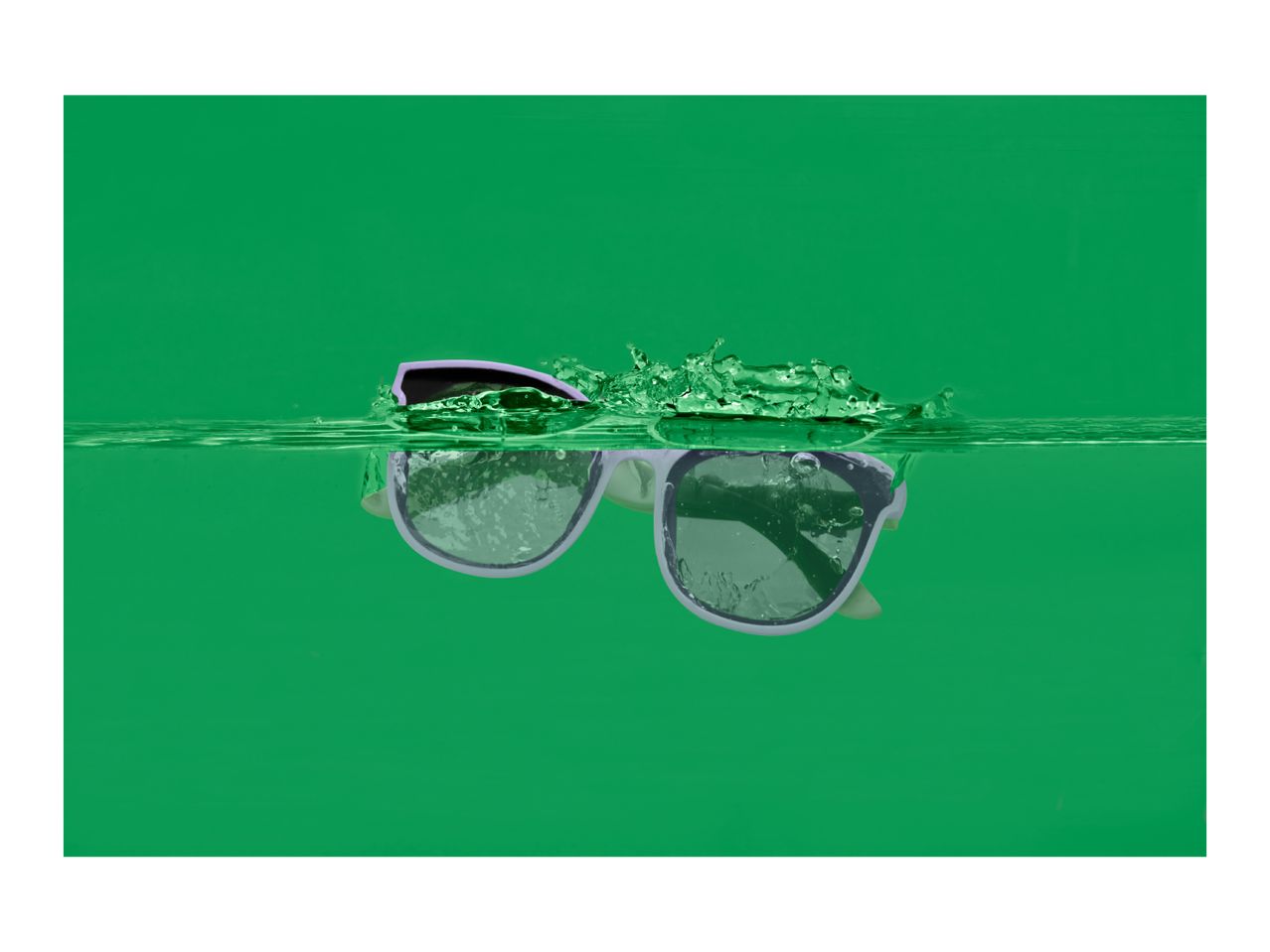 Sunglasses partially submerged in green water with splashes.