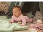 Happy baby in a pink lupilu® sleepsuit with stars, playing on a green blanket.