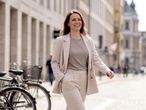 Nő bézs blézerben és nadrágban sétál az utcán, mosolyogva.