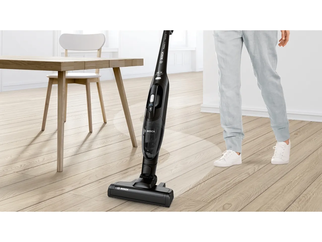 Cordless 2-in-1 vacuum cleaner on a light wooden floor next to a person's legs.