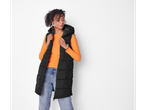 A woman in a black puffer vest, orange long-sleeve shirt, and light-wash jeans.